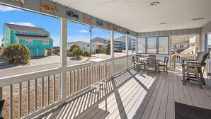 A covered outdoor area with a table and chairs, a view of the street, and a building with a turquoise facade. - Beautiful décor & large private pool! Spacious family home includes decks & huge yard in N. Myrtle. (North Myrtle Beach)