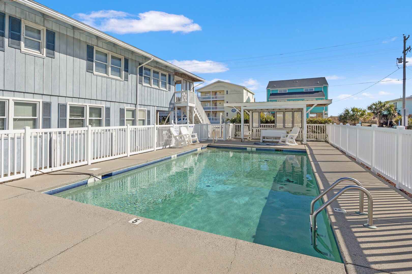 A swimming pool with a white fence, a lifeguard chair, and a lifeguard stand.