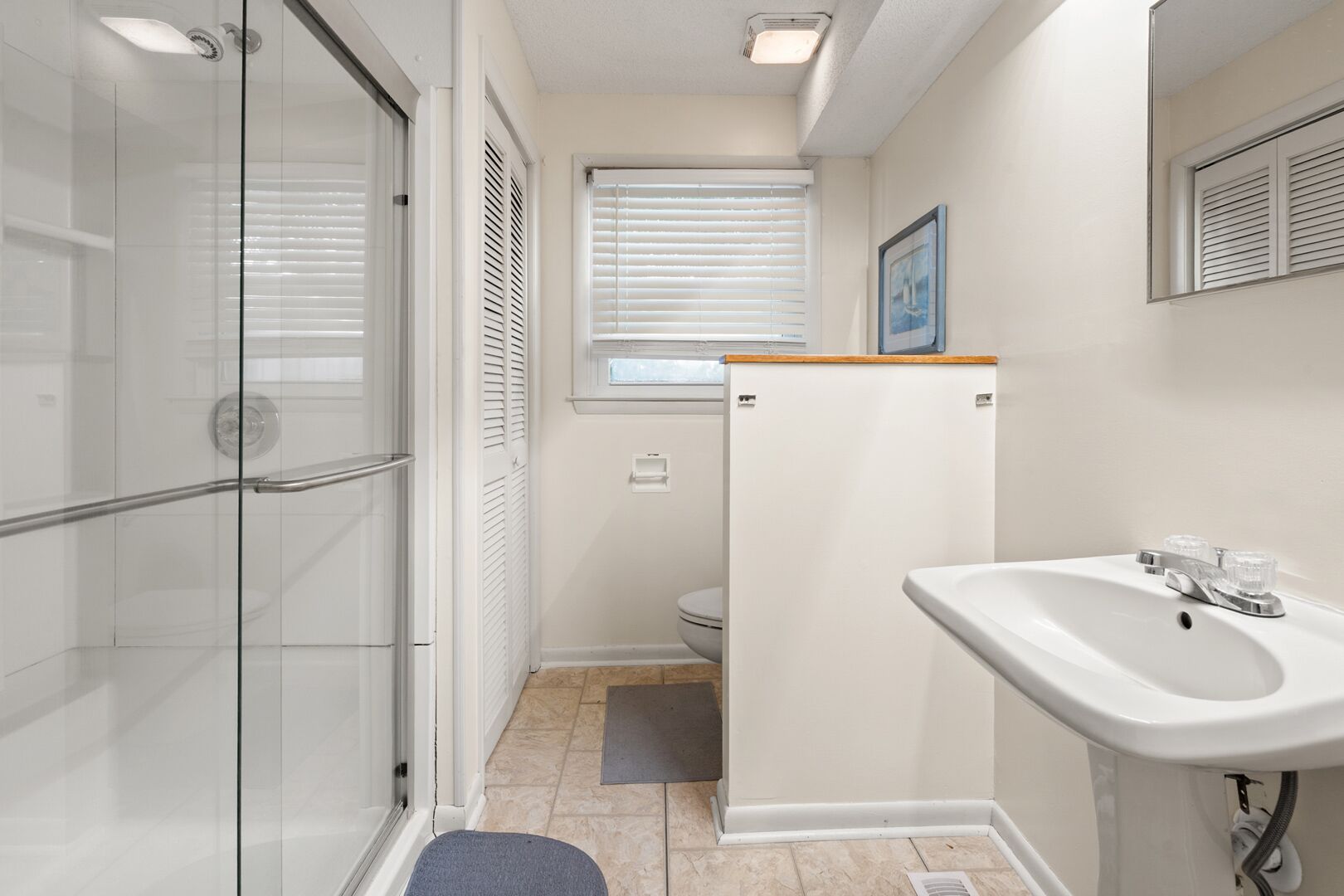 A bathroom with a glass shower enclosure, a toilet, and a sink with a mirror.
