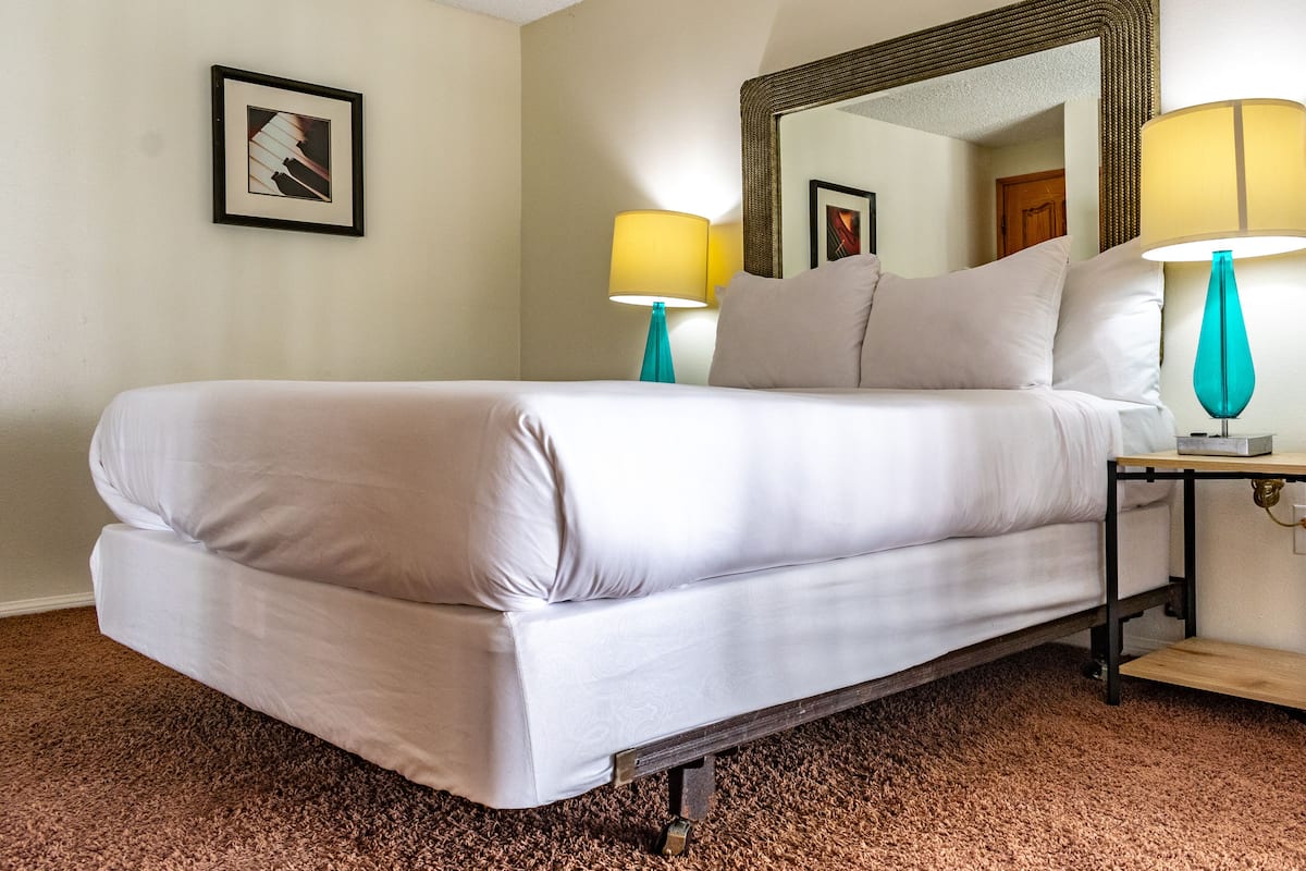 Ein Hotelzimmer mit einem großen Bett, zwei Nachttischlampen, einem Spiegel und einem gerahmten Bild an der Wand.