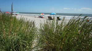 A beach with people relaxing under umbrellas, a sandy shore, and ocean waves. - Your Ultimate Oceanfront Escape! (North Myrtle Beach)