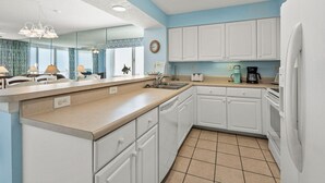 A kitchen with white cabinets, a sink, a coffee maker, and a clock on the wall. - Your Ultimate Oceanfront Escape! (North Myrtle Beach)