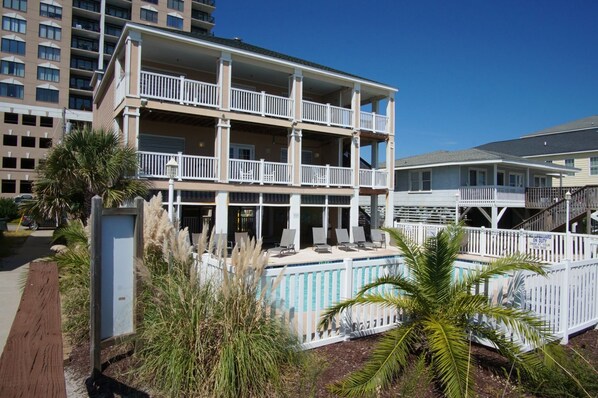 A multi-story hotel with balconies, a swimming pool, and a beach view.