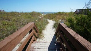 Una passerella in legno che conduce a una spiaggia con sabbia e dune erbose.