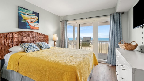 Een slaapkamer met een bed, een schilderij, een televisie, een balkon met uitzicht en een rieten mand.