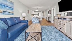 Een moderne woonkamer met een blauwe bank, een houten salontafel en een televisie op een houten kast.