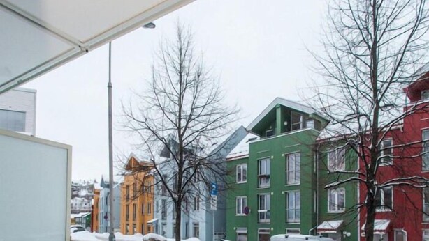 Un balcon doté d’une rambarde en métal, donnant sur une rue enneigée bordée d’immeubles aux couleurs vives.