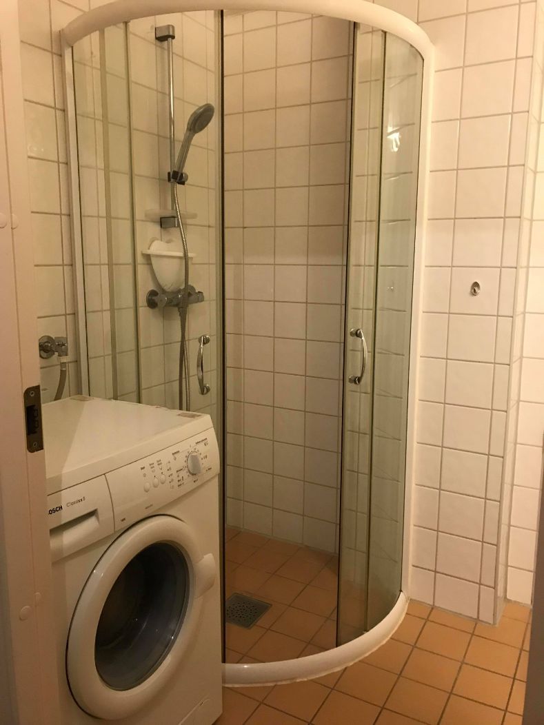 A compact bathroom with a glass-enclosed shower, a washing machine, and tiled walls.