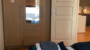 Une chambre avec une armoire en bois, un lit dont les couvertures sont soigneusement pliées, et une porte blanche.