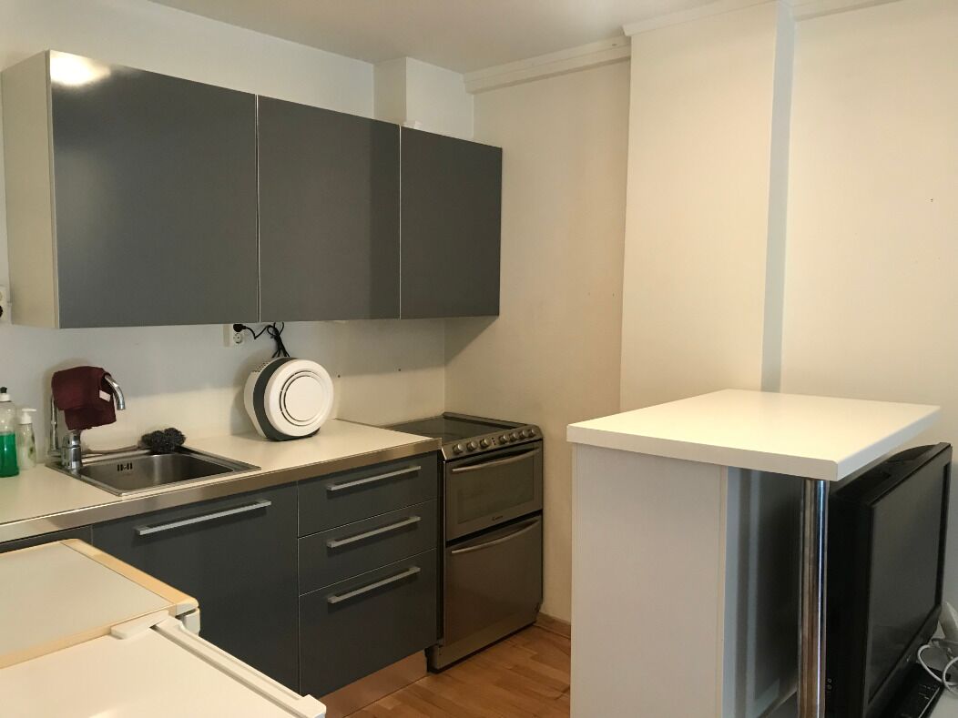 Cocina compacta con gabinetes oscuros, estufa, horno y encimera blanca.