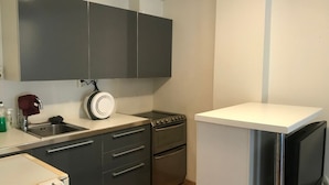 Une cuisine de taille réduite, avec des meubles de couleur sombre, une cuisinière, un four et un plan de travail blanc.