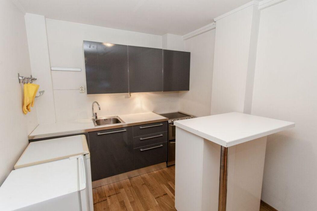 Een compacte keuken met donkere kastjes, een wit aanrecht, een spoelbak en een kleine koelkast.