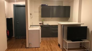 Une cuisine compacte équipée d’un réfrigérateur, d’un four à micro-ondes et d’un téléviseur à écran plat posé sur un meuble.