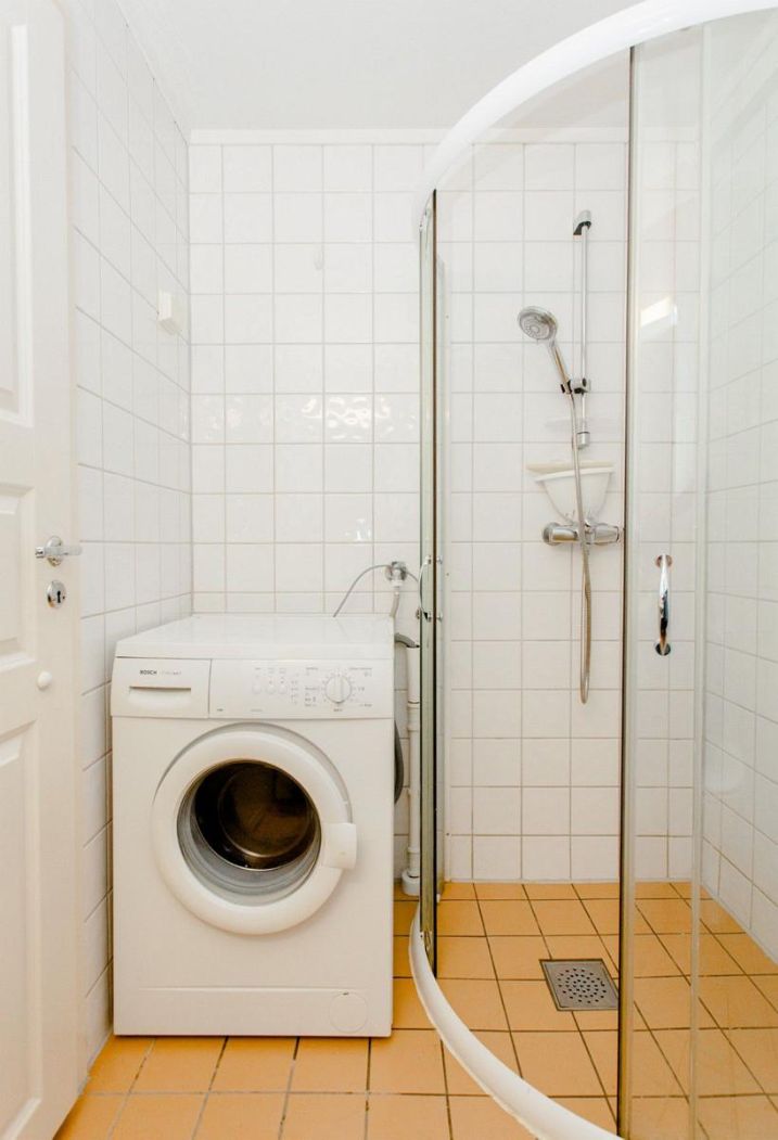 A compact bathroom with a washing machine, a shower enclosure, and a tiled floor.