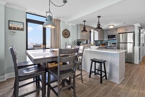 Una cocina moderna con una isla grande, electrodomésticos de acero inoxidable y un comedor con sillas oscuras y una mesa de madera.