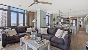 A modern living room with dark leather sofas, a wooden coffee table, and a city view through large windows. - Updated condo with amazing oceanfront view. Pool, sundeck, balconies perfect for couples or families (North Myrtle Beach)