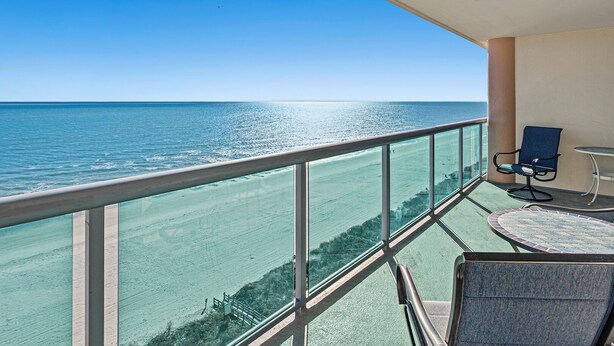A balcony with a clear view of the ocean, a chair, and a small table.