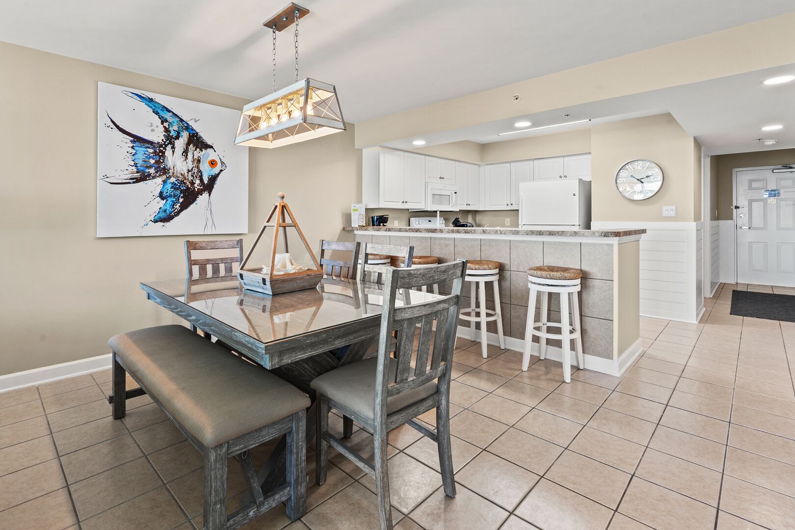 A modern kitchen with white cabinets, a central island, and a dining area with a glass table and wooden chairs.