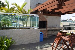 An outdoor patio area with a glass enclosure, a brick wall, and a grill. - Sun Paradise - Beautiful 4 bedroom apartment by the sea (2) (Ponta Verde)