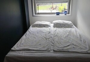 A bed with a white sheet and two pillows, a window with a bicycle outside, and a bowl on the windowsill.