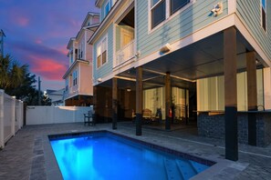 A residential building with a swimming pool, covered patio, and a view of the sky.