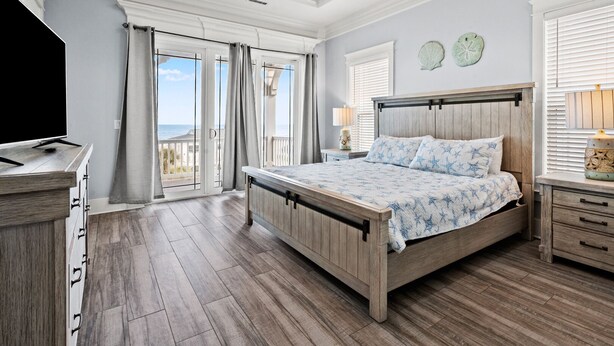 A bedroom with a bed, a TV, a dresser, and a balcony with curtains. - Luxe boulevard home w/private pool, elevator, outdoor kitchen-purely wonderful! (North Myrtle Beach)