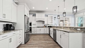 A modern kitchen with white cabinetry, a stainless steel refrigerator, a coffee maker, and pendant lighting. - Luxe boulevard home w/private pool, elevator, outdoor kitchen-purely wonderful! (North Myrtle Beach)