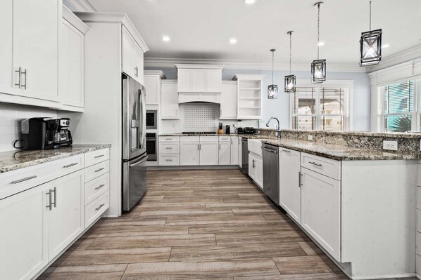 Una cocina moderna con armarios blancos, un refrigerador de acero inoxidable, una cafetera e iluminación colgante.