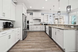 A modern kitchen with white cabinetry, a stainless steel refrigerator, a coffee maker, and pendant lighting.