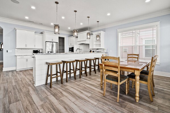 A modern kitchen with white cabinets, a central island, wooden stools, and a dining table with chairs.