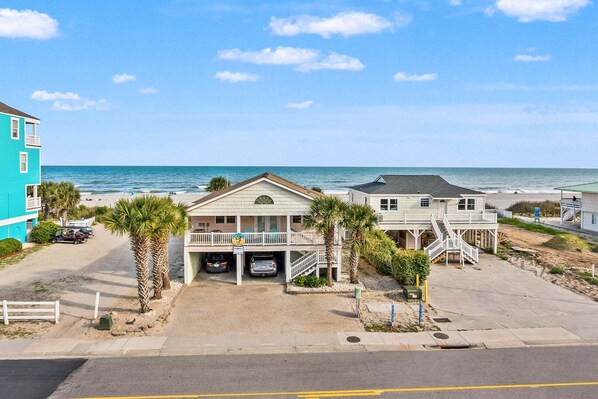 A beachfront property with a two-story building, a covered parking area, and a view of the ocean.