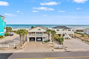 A beachfront property with a two-story building, a covered parking area, and a view of the ocean.