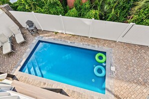 Ein rechteckiger Pool mit weißem Zaun, zwei grünen und einem blauen Schwimmreifen, und einer Pflasterterrasse.