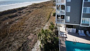 A beachfront property with a pool, outdoor seating, and a view of the beach.