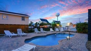 Uma piscina com espreguiçadeiras, cerca e casas ao fundo.