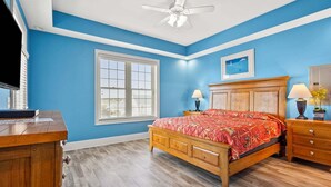 Quarto com cama de madeira, mesa de cabeceira, escrivaninha, ventoinha no teto e janela com persianas.