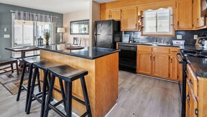 Une cuisine moderne avec des meubles en bois, un réfrigérateur noir, une cuisinière et un grand îlot central doté de tabourets de bar.