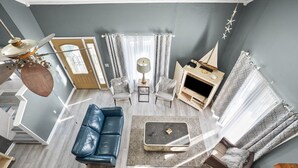 Un salon moderne avec un canapé en cuir bleu, une table basse et un meuble pour la télévision. On y trouve deux fauteuils, une lampe et une maquette de voilier décorative.