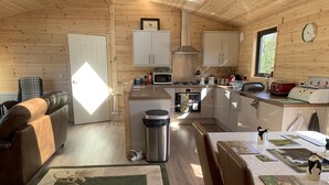 A cozy cabin interior with a dining area, kitchen, and a living room with a sofa and a trash bin. - Smiddyhill Lodge, Innerleithen self catering holiday let (Innerleithen)