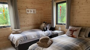 A cozy cabin-style bedroom with two beds, a nightstand, and a window with curtains. - Smiddyhill Lodge, Innerleithen self catering holiday let (Innerleithen)