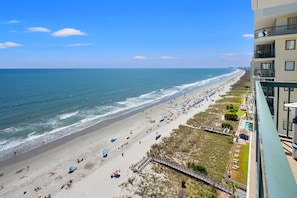 A beach with a wooden walkway leading to a building with balconies.