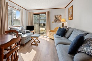 Un salon avec une table à manger en bois, deux canapés, un téléviseur et un balcon avec vue.