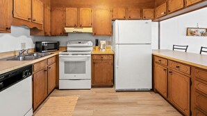 A compact kitchen with wooden cabinets, a white refrigerator, a stove, and a microwave. - Boulevard condo, steps from the beach, w/pool & sundeck, intimate setting for couples & families (North Myrtle Beach)