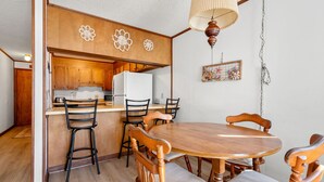 A compact kitchen with wooden cabinets, a white refrigerator, and a dining area with a wooden table and chairs. - Boulevard condo, steps from the beach, w/pool & sundeck, intimate setting for couples & families (North Myrtle Beach)