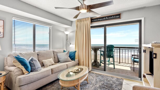 Een woonkamer met een bank, salontafel en uitzicht op het strand door een glazen schuifdeur.