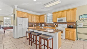 Une cuisine moderne avec des meubles en bois, un îlot central doté de tabourets, un réfrigérateur, un four à micro-ondes et une cuisinière.