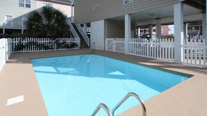 Une piscine rectangulaire entourée d’une clôture blanche et dotée d’une échelle en métal.