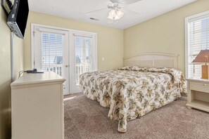 A bedroom with a bed, a desk, a chair, a ceiling fan, and a TV mounted on the wall.