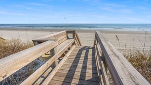 Een houten looppad dat naar een strand leidt, met een helder uitzicht op de oceaan.