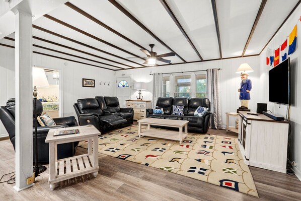 Un salon avec un canapé en cuir noir, une table basse en bois et un tapis à motifs. On y trouve également un téléviseur et une statue posée sur un piédestal.